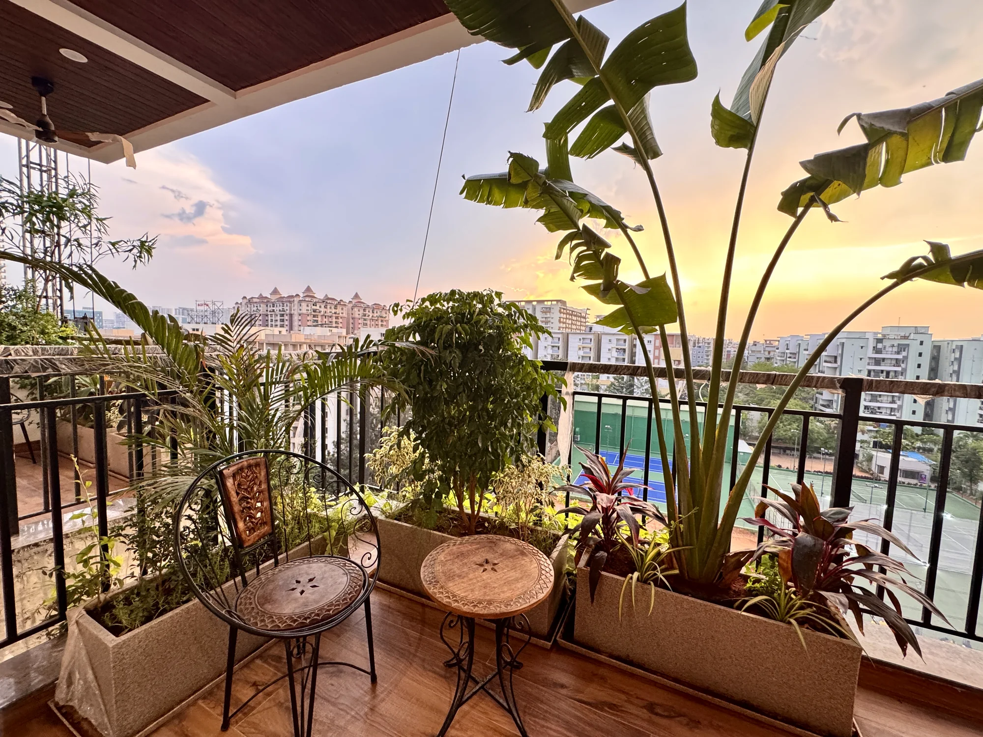 Residential terrace garden with leafy tropical plants, outdoor seating and an open view across the city